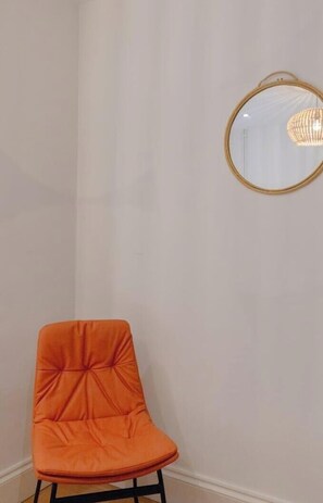 A corner of a room with a single orange chair and a round mirror on the wall.
