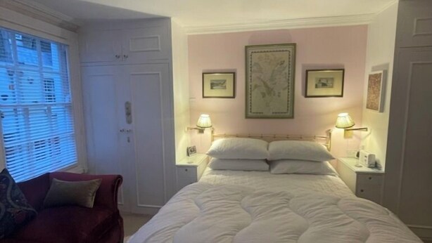 Une chambre à coucher avec un grand lit, deux tables de chevet avec des lampes, un fauteuil rouge et une fenêtre avec des stores.