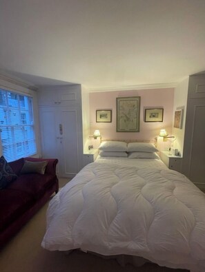 A bedroom with a large bed, two bedside tables with lamps, a red armchair, and a window with blinds.