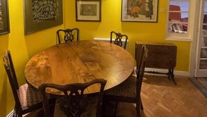 Une salle à manger avec une table ronde en bois entourée de chaises, des murs jaunes et des œuvres d’art encadrées accrochées aux murs.