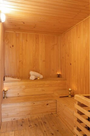 Et sauna-rum af træ med bænke, et håndklæde og stearinlys.