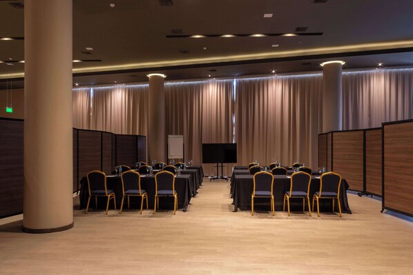A conference room with rows of tables and chairs, a large screen, and a stage.