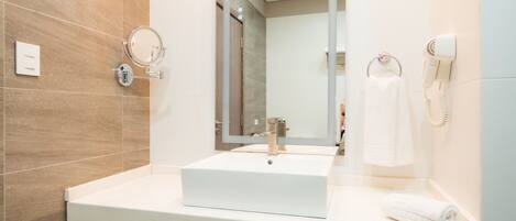 Un baño moderno con un lavamanos blanco, un espejo redondo, un secador de pelo y un perchero para toallas.