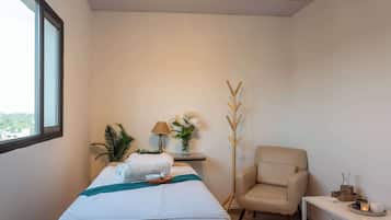 Relax in a serene space with a comfortable bed, a cozy armchair, and a vase with fresh flowers.