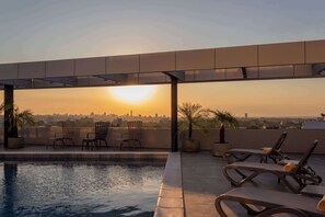 A rooftop pool area with lounge chairs and a view of the city skyline at sunset.