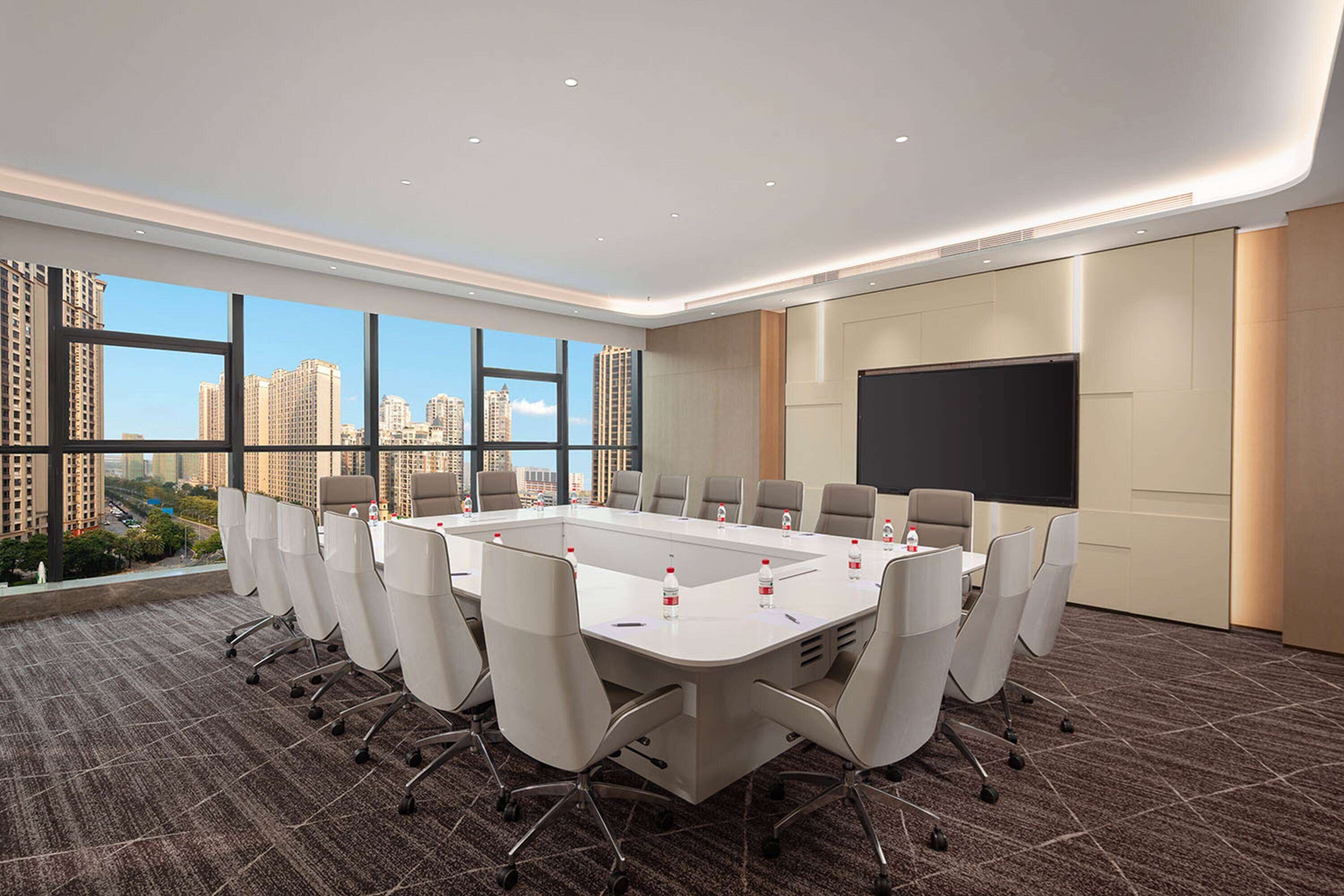 A conference room with a large table, chairs, a projector screen, and a city view.
