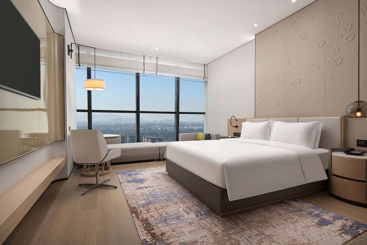 A modern hotel room with a large bed, a desk, and a view of the city.