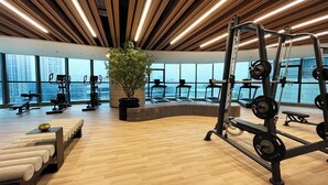 A modern gym with exercise equipment, large windows, and a central seating area with a potted plant. - Wyndham Foshan Nanhai (Foshan)