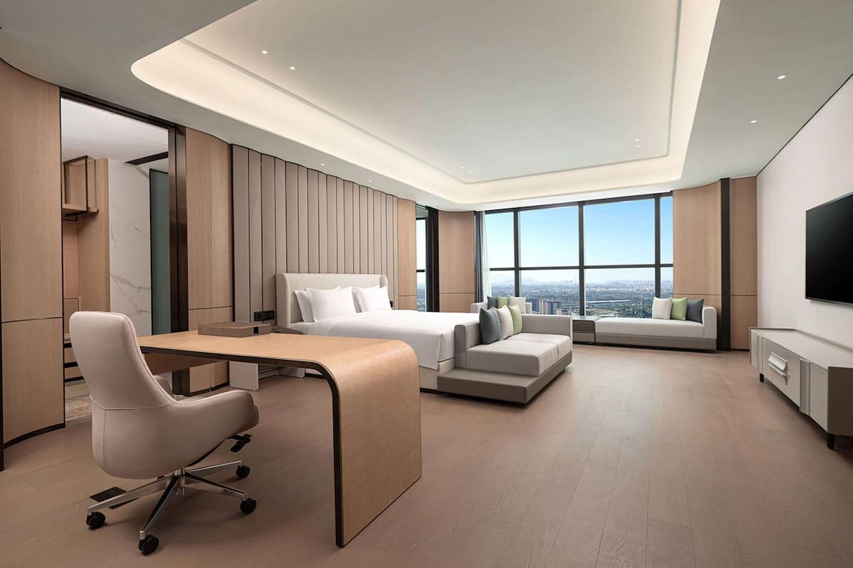 A modern hotel room with a large bed, a desk, a sofa, and a TV.