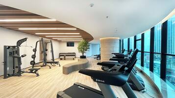 A modern gym with cardio equipment, weight machines, and a large window offering a city view.