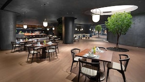A modern restaurant with wooden tables and chairs, a bar area, and a central tree. - Wyndham Foshan Nanhai (Foshan)