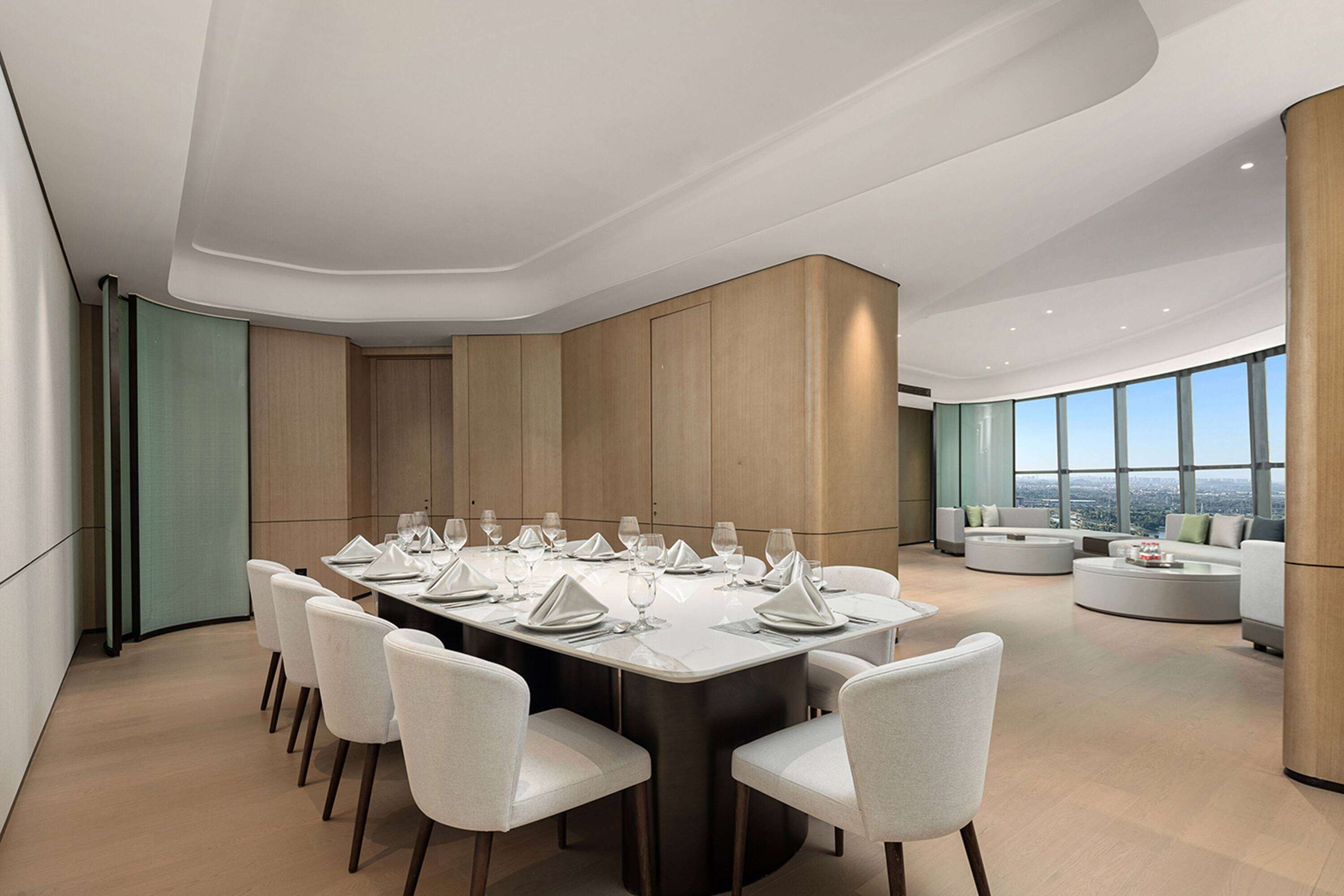 Un espace repas moderne avec une longue table dressée pour un repas, entourée de chaises blanches, et un coin salon avec des canapés et une table basse.