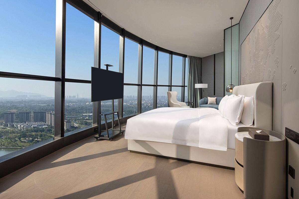 A modern hotel room with a large bed, a TV, and a view of the city.