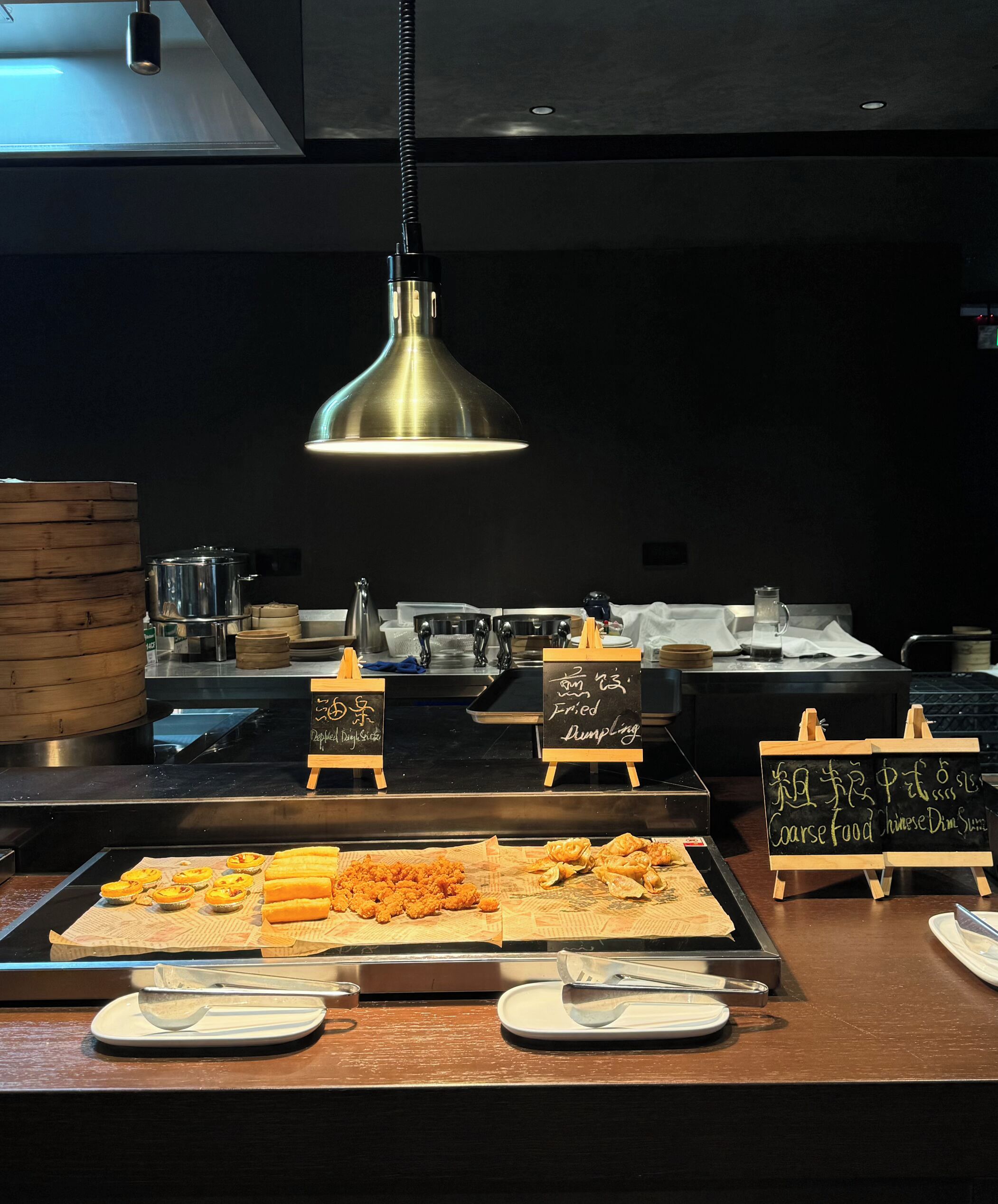 A buffet counter with various dishes and food items displayed on trays, accompanied by small chalkboards with food names.