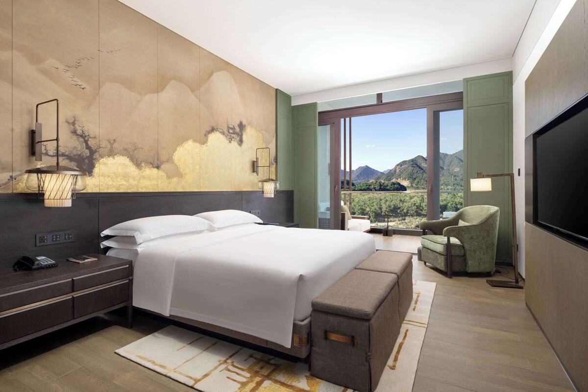 Una habitación de hotel moderna con una cama grande, un escritorio con lámpara, una silla y un televisor.