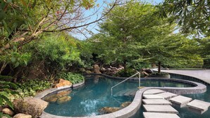 A serene outdoor pool area with a curved design, surrounded by lush greenery and rocks. - Wyndham Fuzhou Guian (Fuzhou)