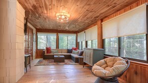 Une pièce spacieuse avec un plancher en bois, une grande fenêtre, un canapé, un fauteuil et un meuble.