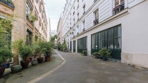 Une rue étroite bordée de plantes en pot et de bâtiments dotés de grandes fenêtres.