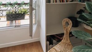 Une pièce dotée d’une grande fenêtre, d’une bibliothèque et d’un fauteuil en osier.