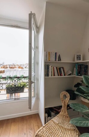 A room with a large window, a bookshelf, and a woven chair.