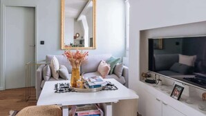 Un salon moderne avec un canapé blanc, une table basse, un grand miroir et un téléviseur fixé au mur.