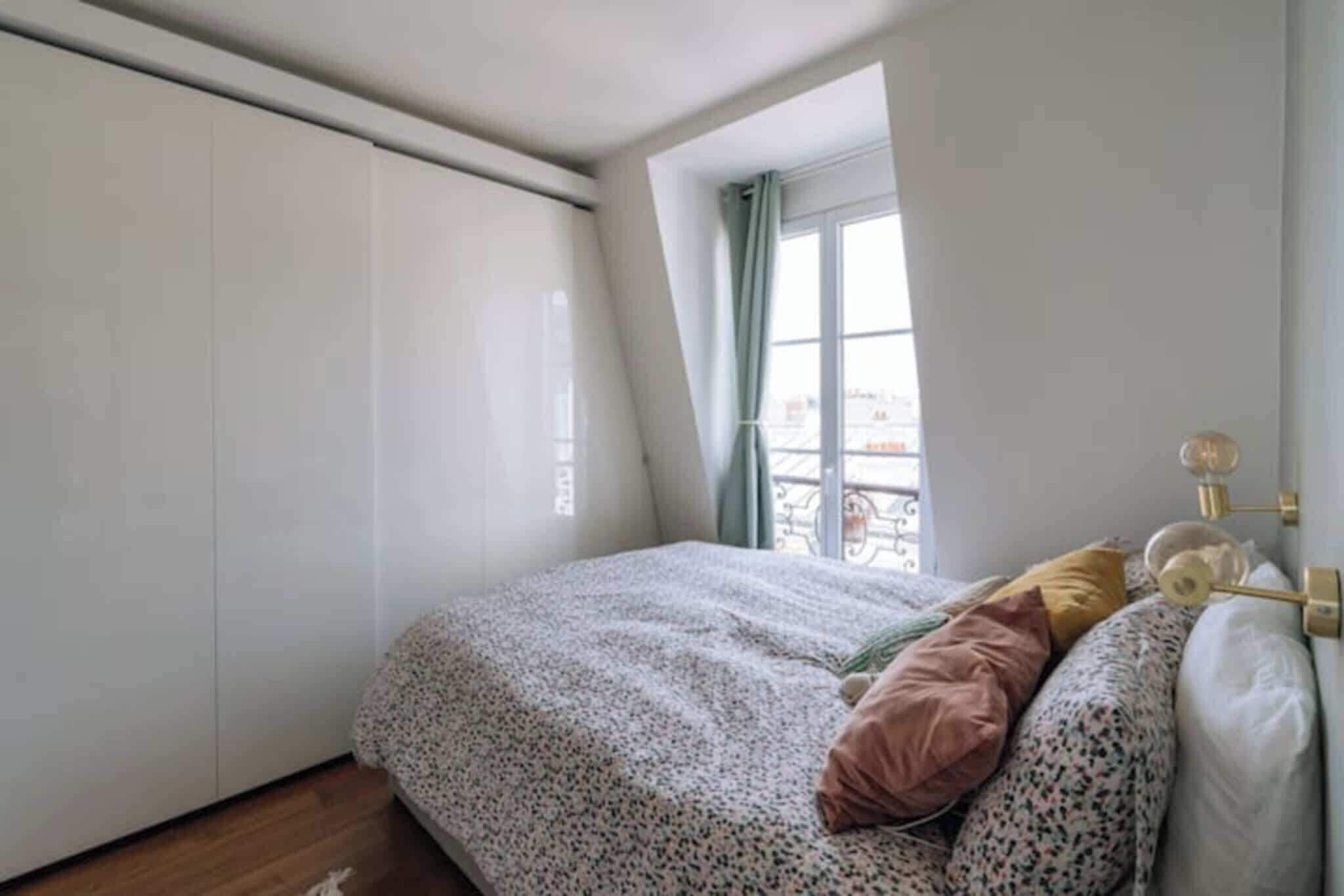 A bedroom with a bed, pillows, a window, and a wardrobe.