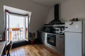 Une cuisine compacte équipée d’un four encastré, d’un réfrigérateur et d’une fenêtre donnant sur un quartier résidentiel.