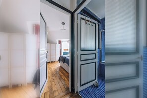 Een kamer met een bed, een raam met jaloezieën en een deur die naar een andere kamer leidt.
