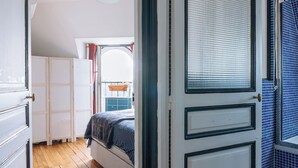Ein Schlafzimmer mit Holzboden, einem Bett mit blauer Decke, einer weißen Tür mit Fenster und einer Wand mit blauen Fliesen.