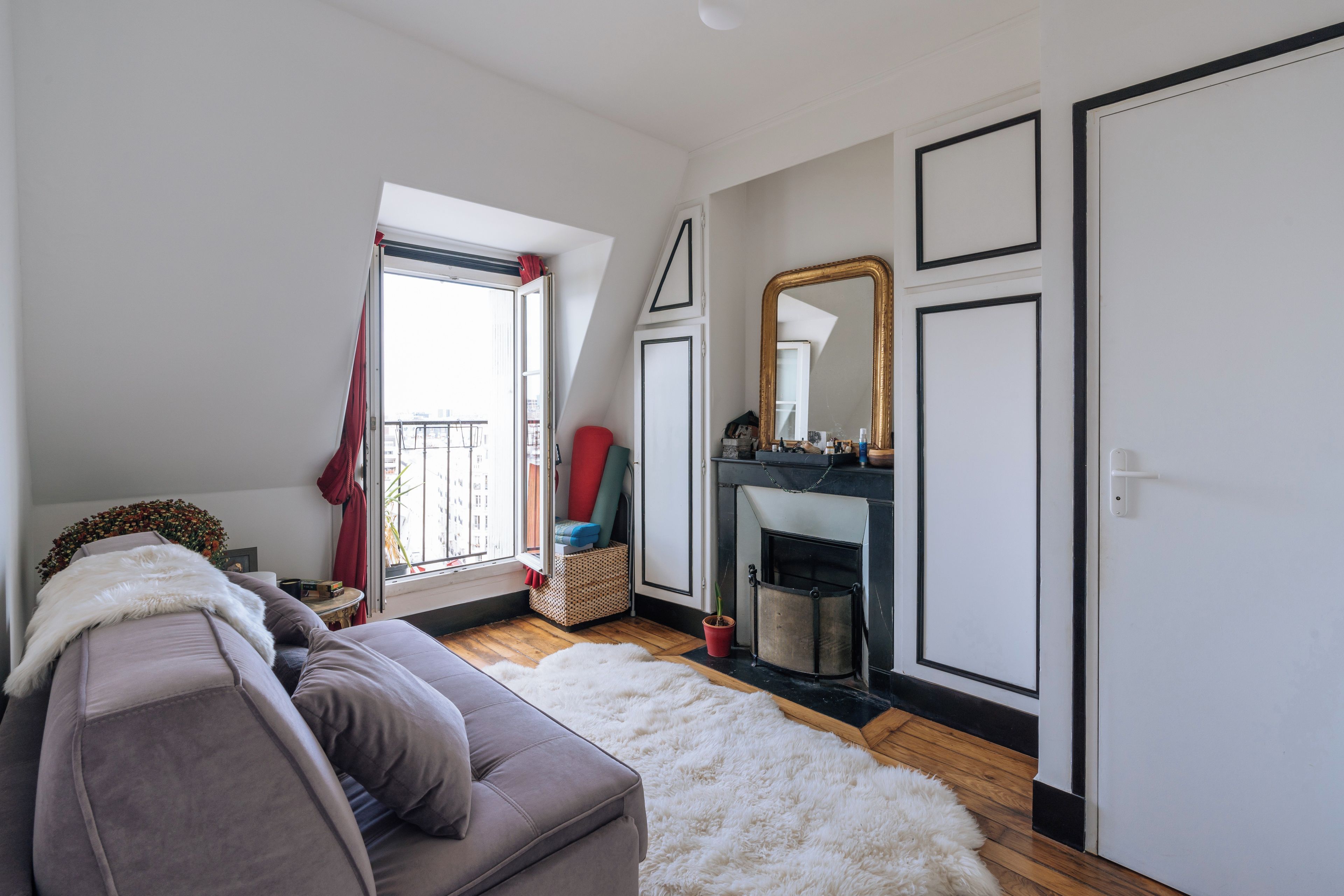 Un salon moderne avec un canapé gris, un tapis blanc et moelleux, une cheminée et un grand miroir au mur.