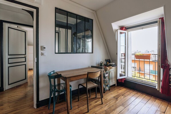 A room with a wooden desk, two chairs, a window with a view of buildings, and a door leading to another room.