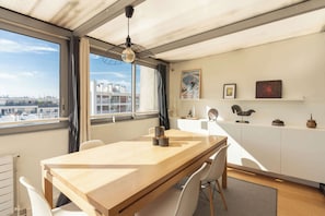 Eine moderne Küche mit einem Holztisch, weißen Schränken und Blick auf die Stadt durch große Fenster.