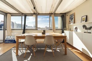 A modern room with a large table, four chairs, a view of the city, and a wooden ceiling.