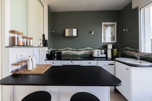 A modern kitchen with a black countertop, white cabinets, a stainless steel range hood, and a tiled backsplash.