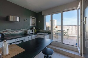 A kitchen with a black countertop, a stainless steel range hood, a tiled backsplash, a window with a view of a balcony, and a door leading to an outdoor area.