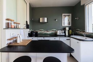 Eine Küche mit schwarzem Arbeitsplatz, weißen Schränken, einer Edelstahl-Dunstabzugshaube, einer Kaffeemaschine und einem Vintage-Poster an der Wand.