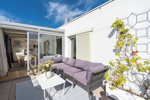 A modern patio with a wicker sofa, a white table, and a potted plant. - Breathtaking 2BR – Buttes Chaumont & Terraces (Paris)