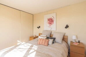 A bedroom with a bed, bedside tables, a wall-mounted lamp, and a painting. - Breathtaking 2BR – Buttes Chaumont & Terraces (Paris)