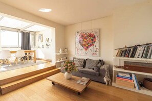A living room with a sofa, coffee table, and a bookshelf. - Breathtaking 2BR – Buttes Chaumont & Terraces (Paris)