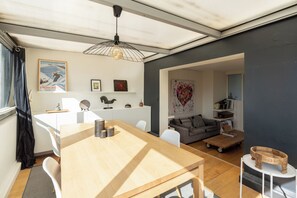 A modern living space with a wooden dining table, a gray sofa, and a large window.