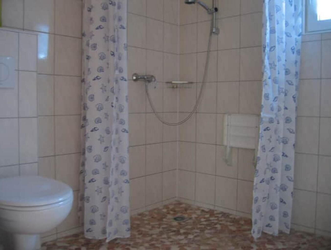 Ein kleines Badezimmer mit Toilette, Dusche und Fliesenboden.