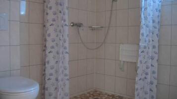 Ein kleines Badezimmer mit Toilette, Dusche und Fliesenboden.