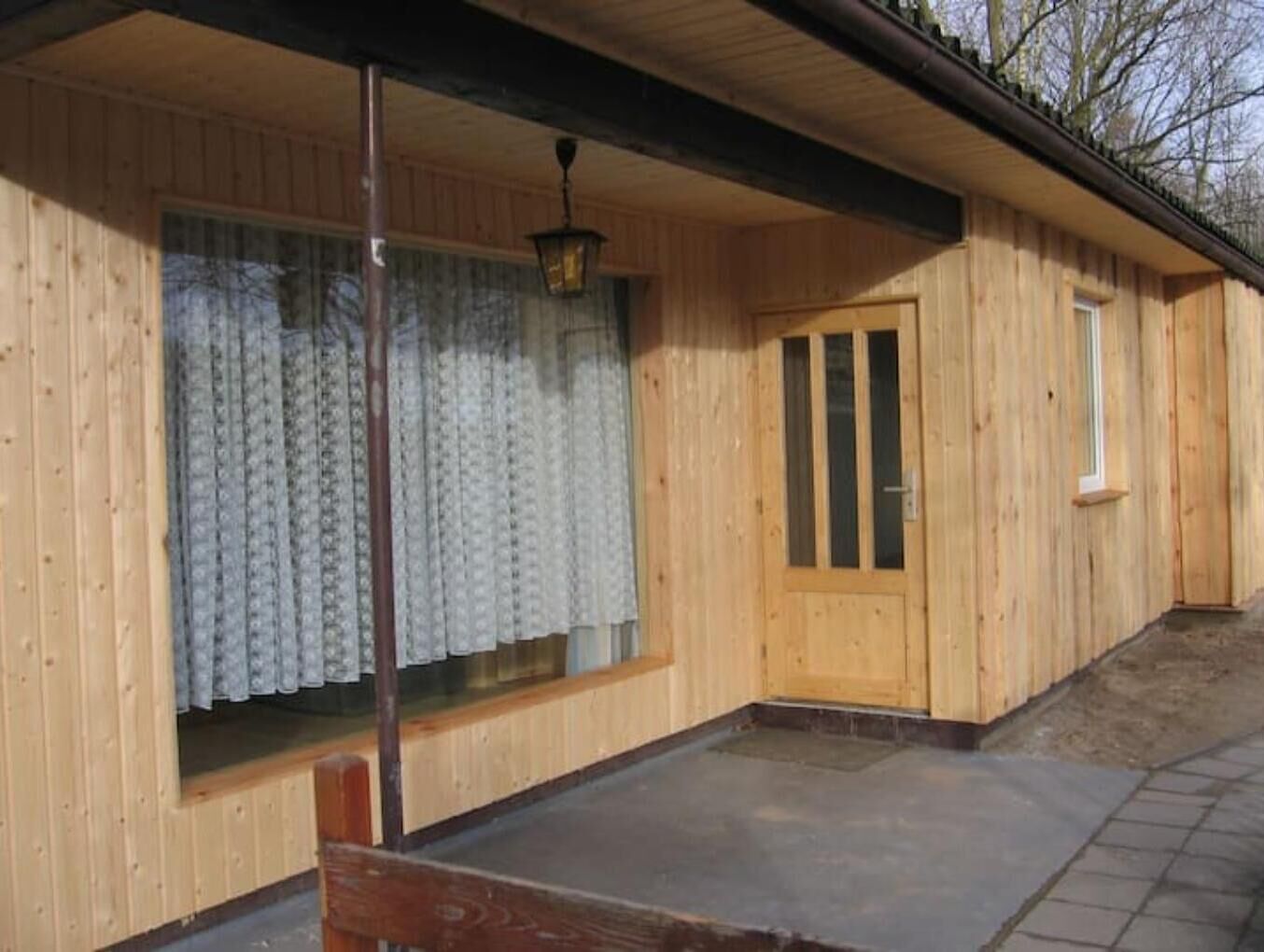 A wooden cabin with a covered porch, a window with curtains, and a door.