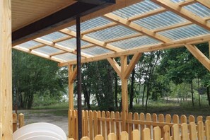 Ein hölzernes Pavillon mit Metalldach, umgeben von einem Holzzaun, inmitten eines bewaldeten Gebiets.