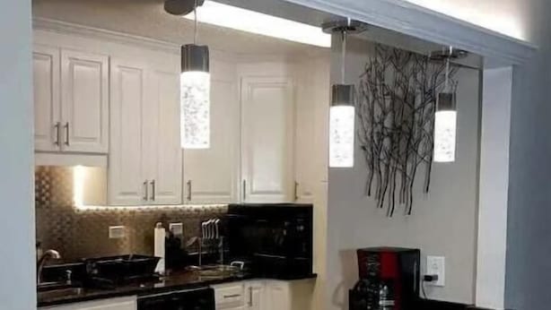 Una cucina moderna con mobili bianchi, un piano di lavoro in granito, una macchina da caffè e un elemento decorativo a parete.