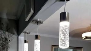 Una cucina moderna con piani in granito, illuminazione a sospensione e zona pranzo con una sedia rossa e una pianta.