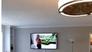 Un soggiorno con una televisione a schermo piatto montata a parete, un divano giallo, un tavolino da caffè in vetro, una lampada e un piccolo tavolino laterale.