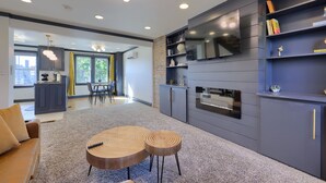 A modern kitchen with a built-in TV, grey cabinetry, and a dining area with a table and chairs. - Modern Downtown Lancaster Apt – Walk to Train & Amtrak (Lancaster)