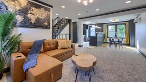 A spacious living area with a brown leather sofa, a round coffee table, and a large abstract painting on the wall. - Modern Downtown Lancaster Apt – Walk to Train & Amtrak (Lancaster)