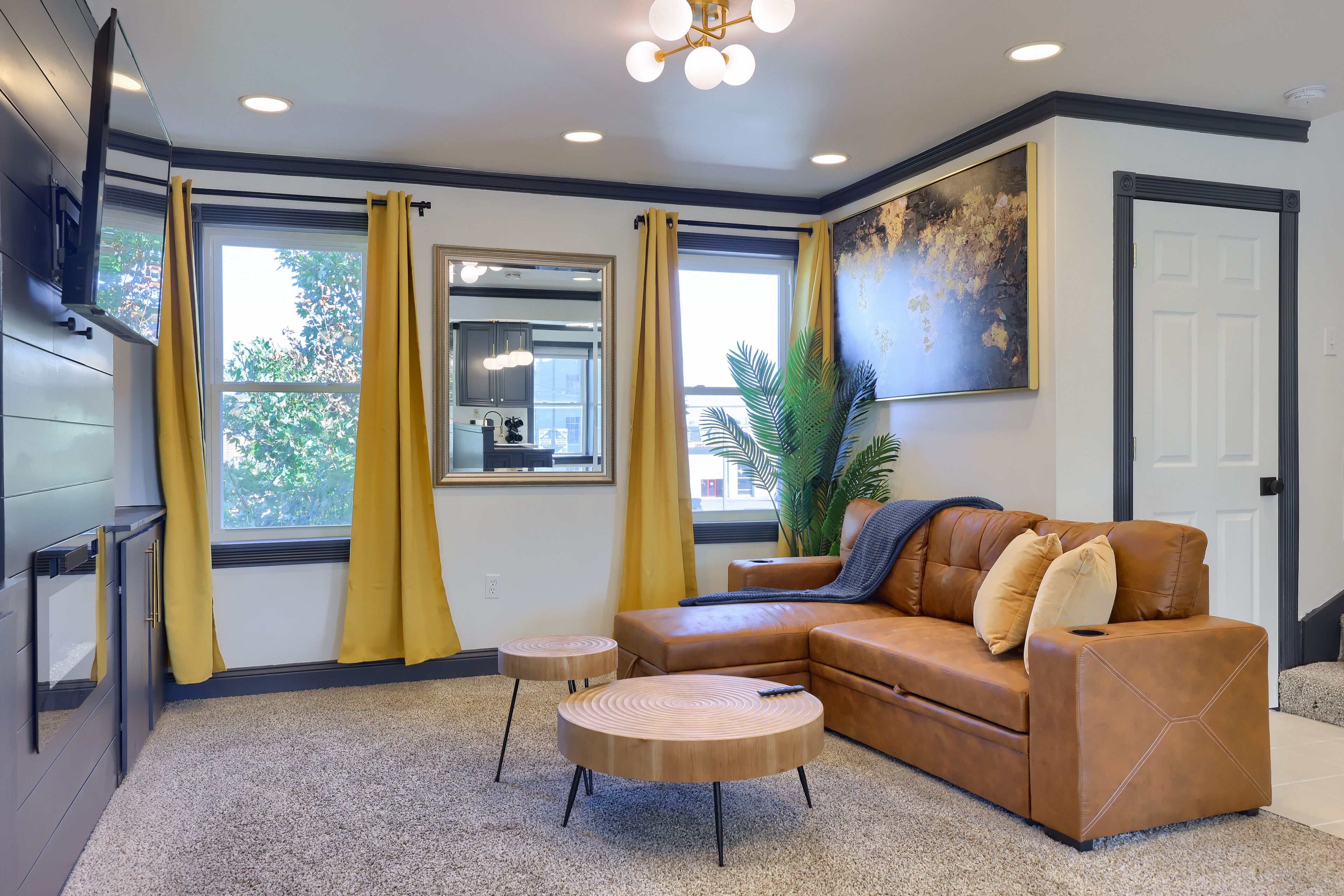 A modern living room with a brown leather sofa, two round wooden coffee tables, and yellow curtains.